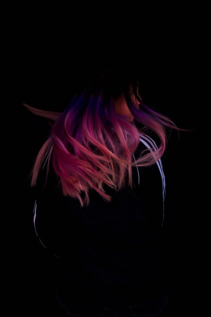 Dynamic image of person with pink and purple hair in motion against dark background.